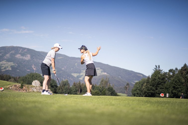 Servizi premium per il golf nel nostro hotel in Alto Adige Due donne che giocano a golf su un campo verde con montagne sullo sfondo